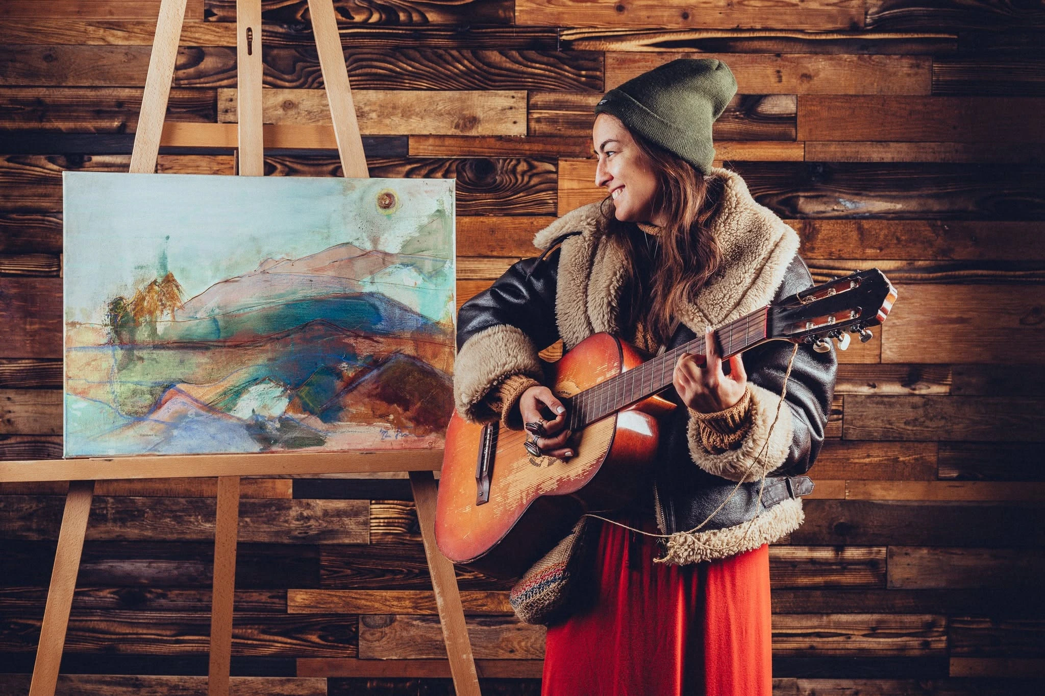 Zuzana smiling with her guitar beside an original painting